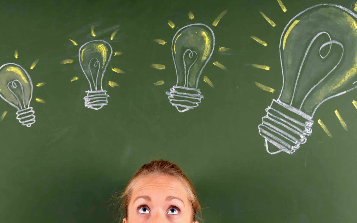 Frau schaut nach oben zu mit Kreide gezeichneten Glühbirnen auf einer grünen Tafel