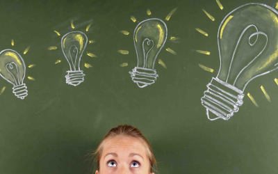 Frau schaut nach oben zu mit Kreide gezeichneten Glühbirnen auf einer grünen Tafel