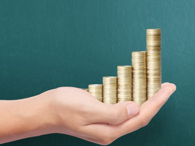 Hand hält gestapelte Goldmünzen in aufsteigender Reihenfolge, symbolisiert finanzielles Wachstum